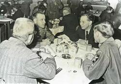 ["Black and white photograph print of Carl Albert seated at a table with three other gentlemen during the trip to Korea."]