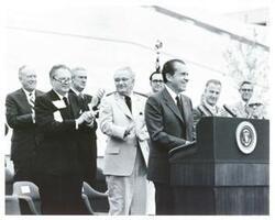 ["Black and white photograph print of Richard M. Nixon speaking at the dedication of the Lyndon B. Johnson library. Also shown is William P. Rogers, John Connally, Lyndon B. Johnson, and Spiro Agnew."]