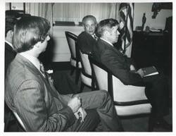 ["Black and white photograph print of several unidentified men seated in chairs."]
