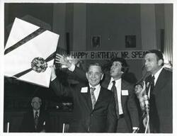 ["Black and white photograph print of Carl Albert holding up one of his birthday presents. Tom Steed and Ray Harris are also shown."]