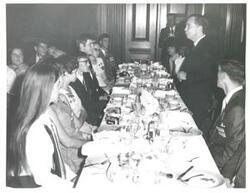 ["Black and white photograph print of Carl Albert speaking to several people seated at a dinner table."]