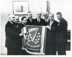 ["Black and white photograph print of Carl Albert, John W. McCormack, Michael Kirwan, and several other men holding a rug that says: Erin Go Bragh."]