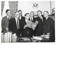 ["Three identical black and white photograph prints, and the negative, of Carl Albert with Sen. David Boren and a group of unidentified men, looking at a booklet, The Seminole Tribal Cultural Center"]