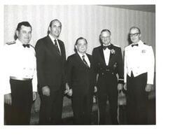["Black and white photograph of Carl Albert posing for a photo, along with four other unidentified men, at the United States Naval League Council in McAlester, Oklahoma on Armed Forces Day 1976."]