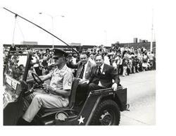 ["Black and white photograph of Carl Albert and Henry Bellmon riding in a jeep on Armed Forces Day in McAlester, Oklahoma on May 15, 1976"]