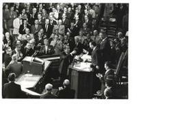 ["Black and white photograph of a group of men in the House chamber. Carl Albert, Gerald Ford, and Richard M. Nixon are pictured."]