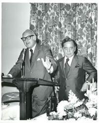 ["Carl Albert standing behind a speaker at a podium."]